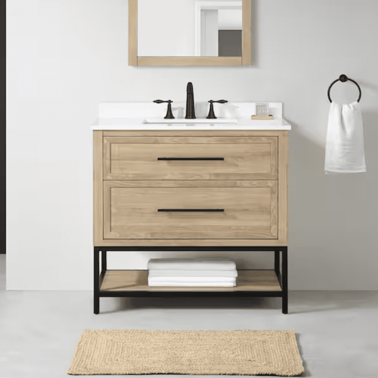 Light wood bathroom vanity with black hardware, white countertop sink, and open shelf at the bottom