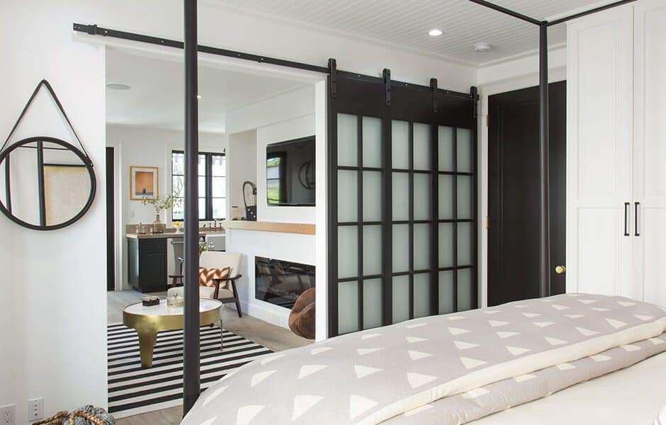 Modern bedroom with sliding doors, round mirror, and view of sitting area with fireplace