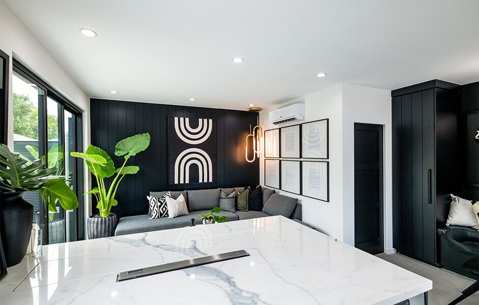 Modern living room with black accent wall, gray sofa, plants, and marble countertop
