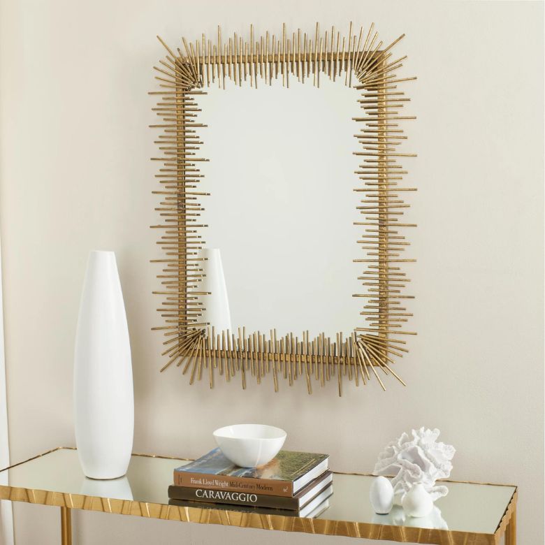 Gold sunburst-framed mirror above a console table with white vase, books, and decorative accents