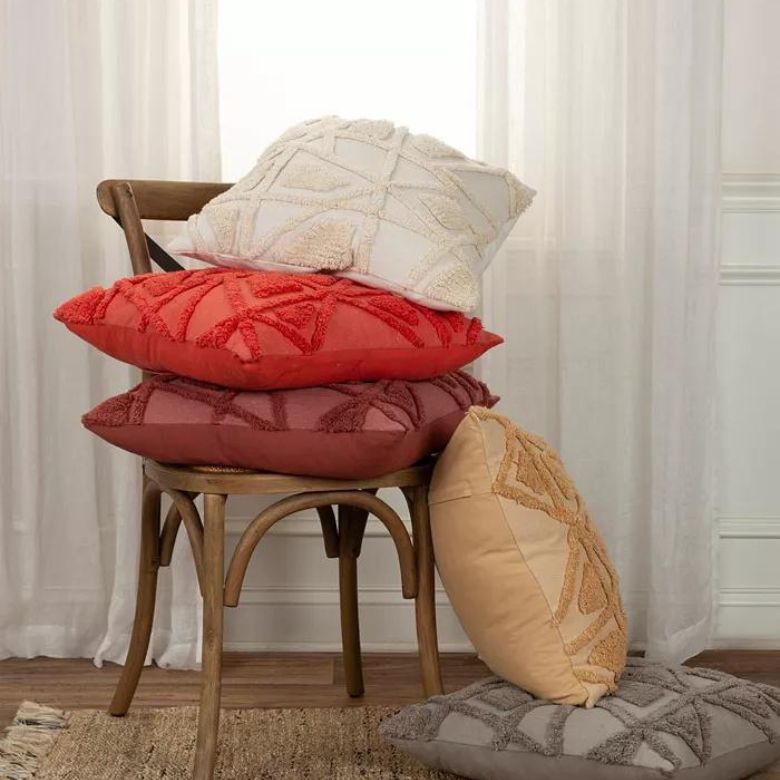 Colorful textured throw pillows stacked on a wooden chair in front of sheer curtains