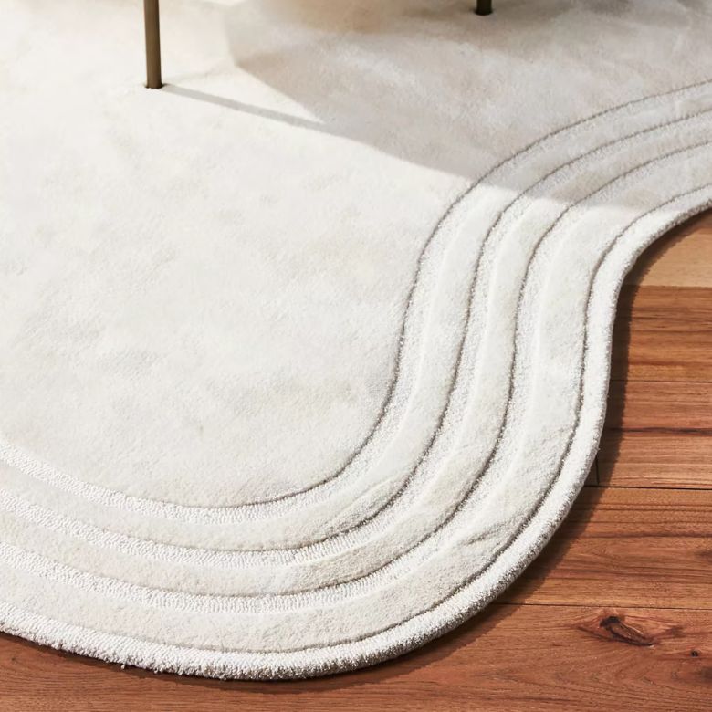 Curved white area rug with textured border on wooden floor