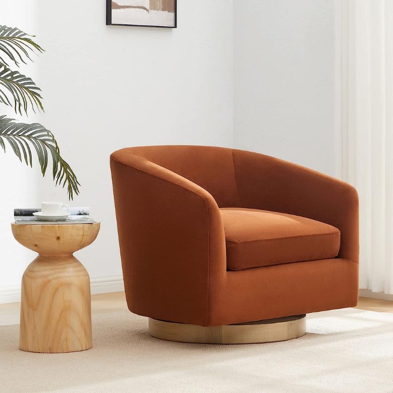 Rust-colored swivel armchair with a wooden accent table on a light rug, surrounded by minimal decor and greenery
