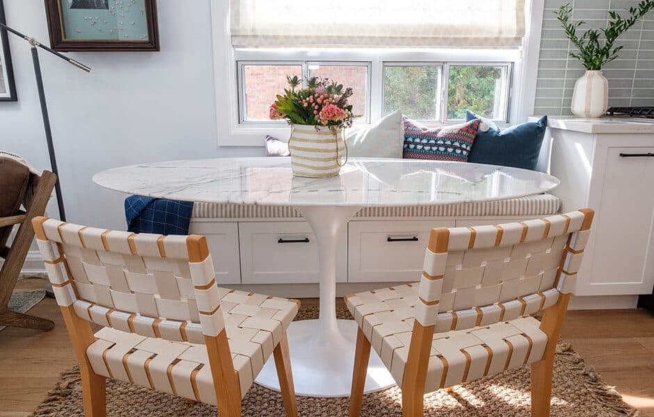 Cozy dining nook with marble table, woven chairs, and window bench seating with colorful pillows