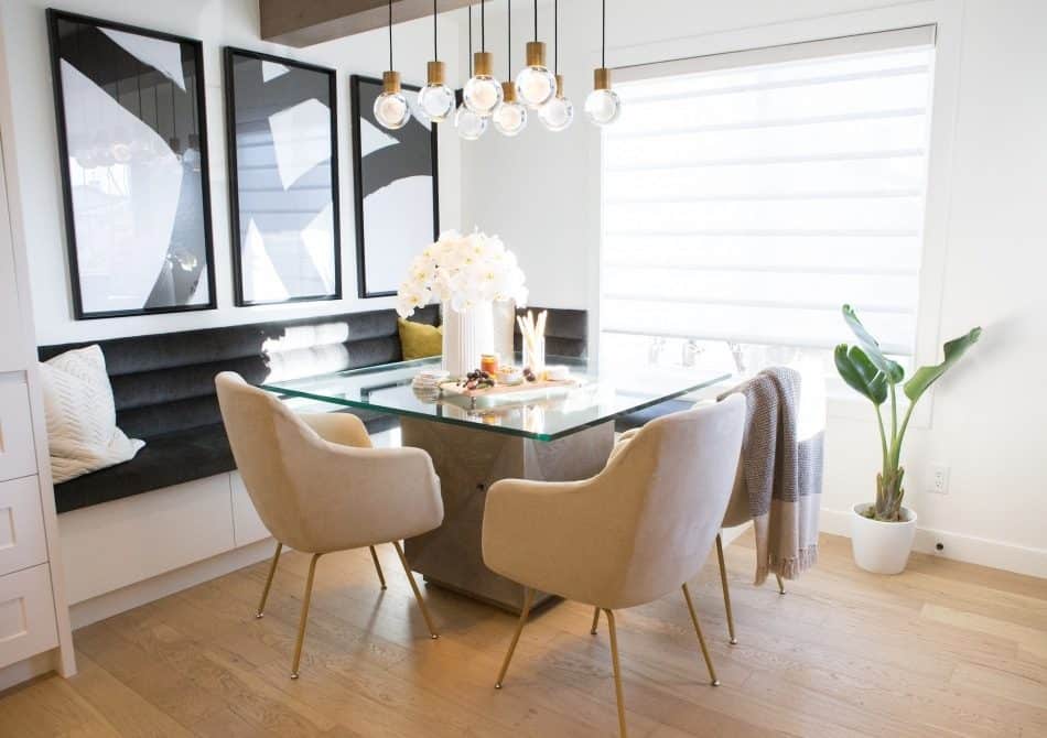 Bright dining area with glass table, beige chairs, black bench, pendant lights, and white flowers