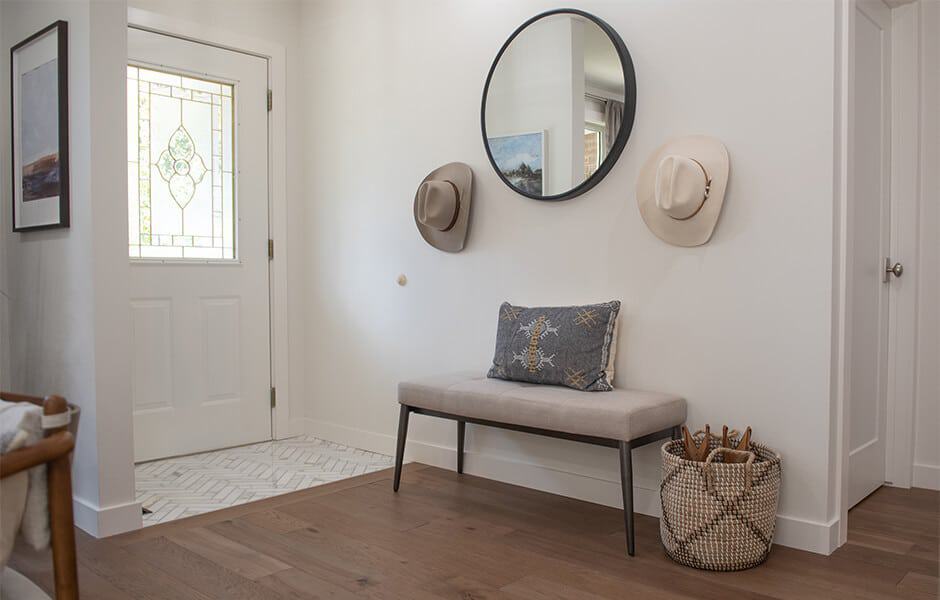 Bright entryway with bench seating, round mirror, and decorative accents including hats and a woven basket
