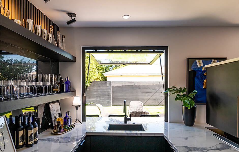 Modern home bar with open window, marble countertops, and stylish glassware