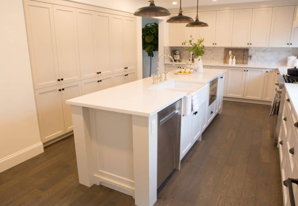 A renovated kitchen with a large white island, pendant lights, built-in cabinets, and stainless steel appliances