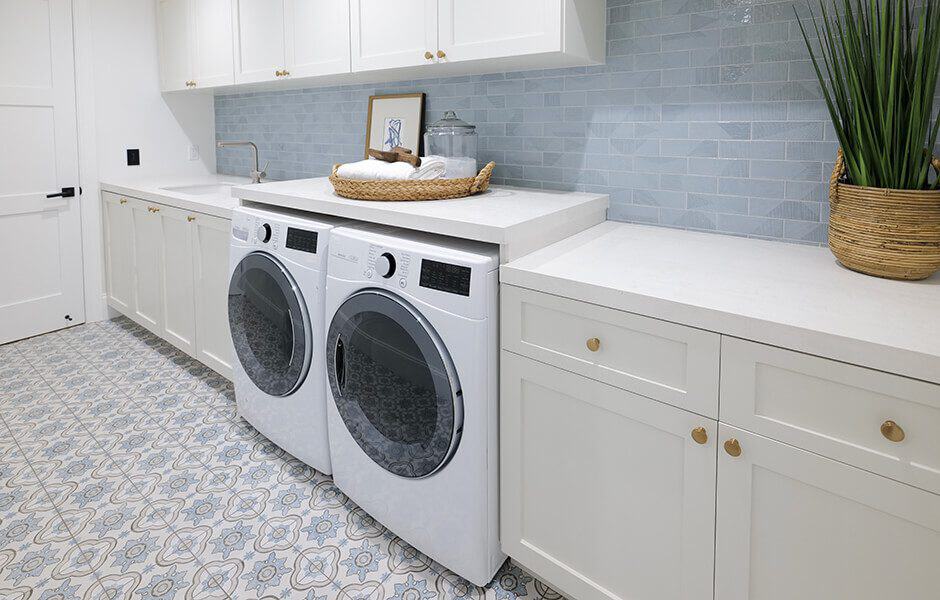 Renovated laundry room with white cabinets, a tiled backsplash, and front-loading washer and dryer
