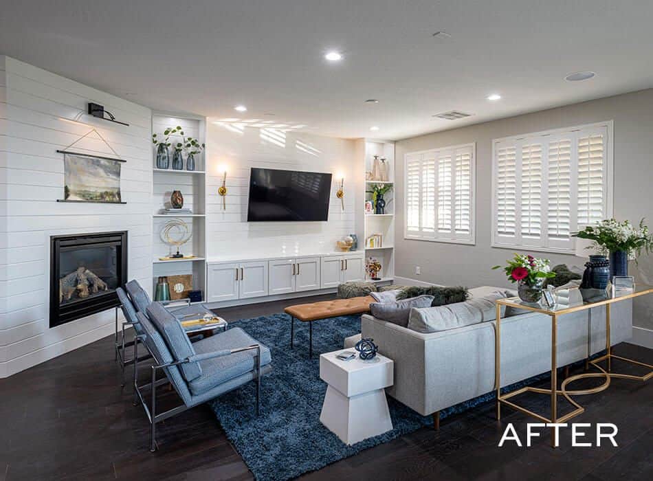 An after image of a renovated living room with white fireplace, mounted TV, gray sofa, dark wood floor, white shutters
