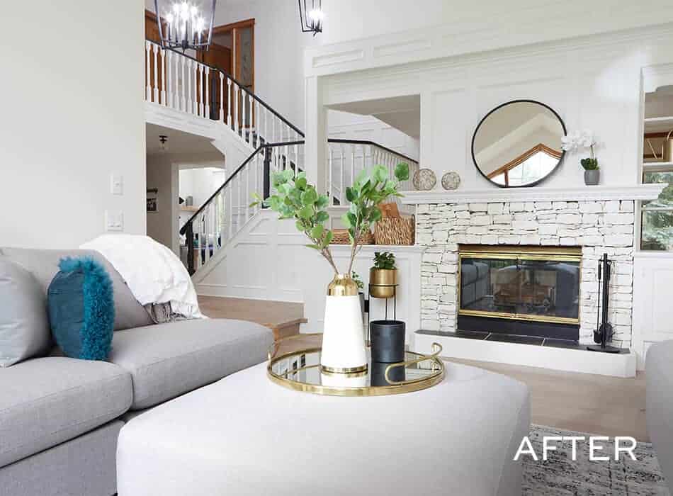 Modern living room with a gray sectional sofa, white ottoman, decorated mantel, and a stone fireplace