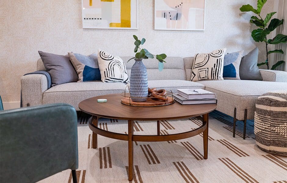 Modern living room with a gray sectional, patterned pillows, a round wooden coffee table, and abstract wall art