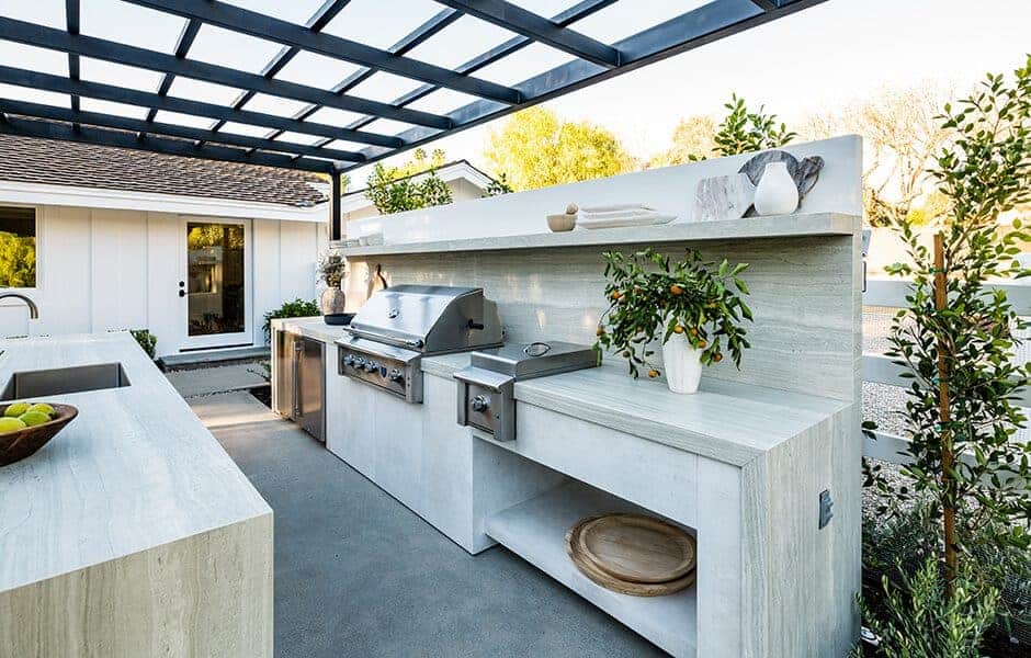 Modern outdoor kitchen with built-in grill, sink, stone counters, and pergola-style roof
