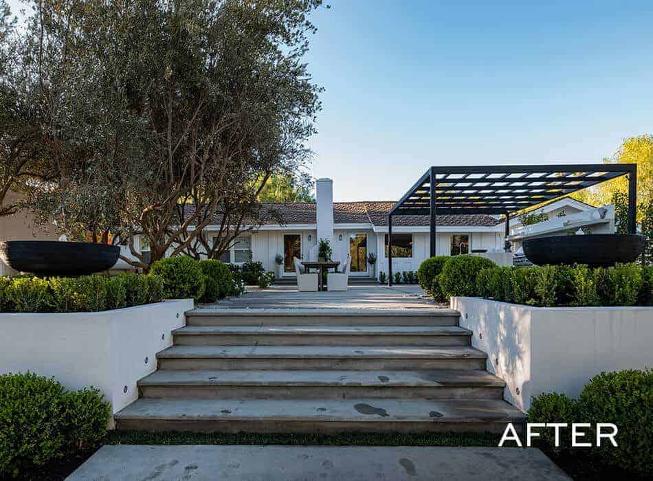 Elegant outdoor entry with stone steps, modern landscaping, large planters, and a pergola-covered kitchen area