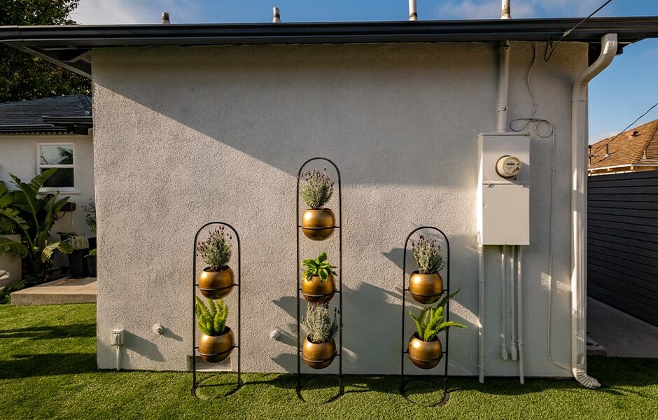 Wall-mounted black metal plant stands with gold pots holding lavender and greenery