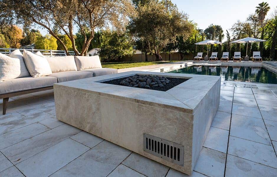 Stone fire pit with black lava rocks beside a pool, surrounded by lounge chairs and cushioned outdoor seating