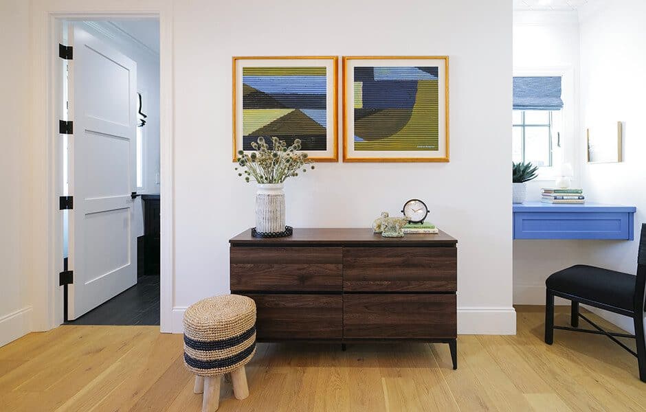 Modern bedroom with white walls, a dresser, a stool, and two framed abstract paintings
