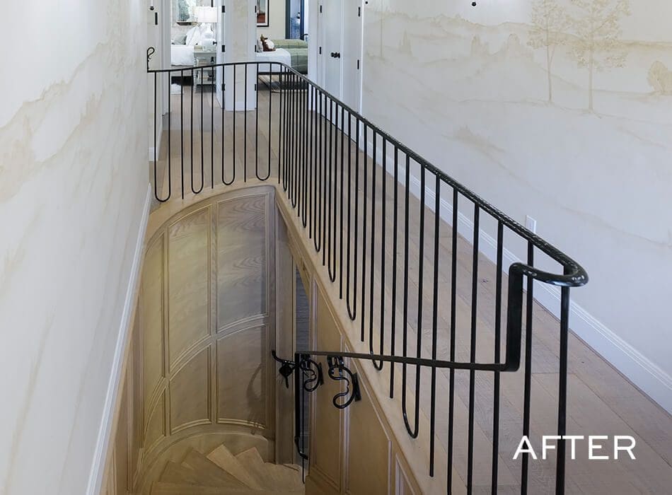 Hallway with light wood floors, decorative wall mural, and black wrought iron railing along a staircase