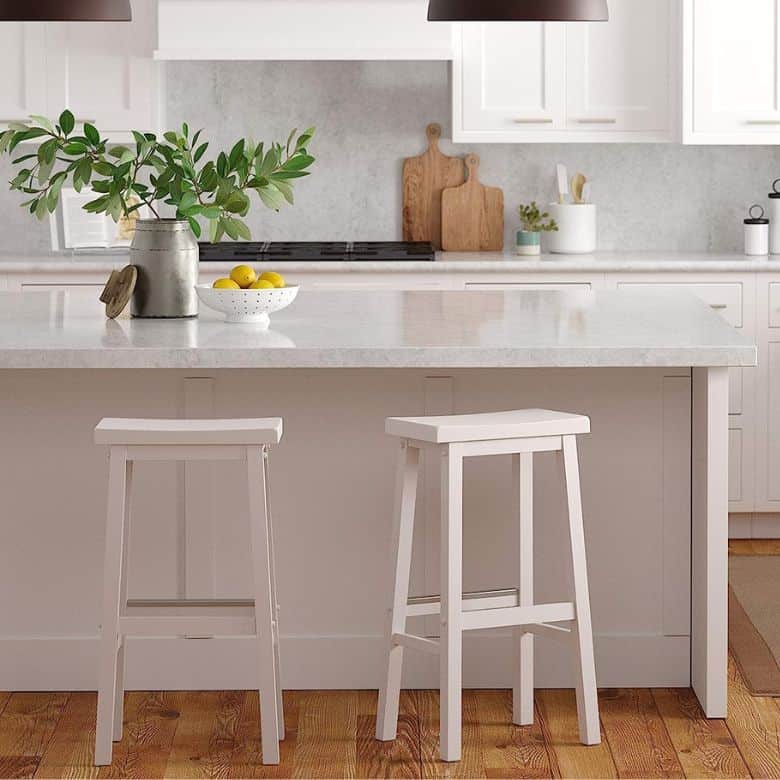 Bright kitchen with white cabinets, a marble island countertop, two white bar stools, and wooden cutting boards as decor