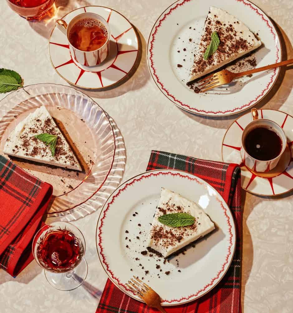 Cheesecake slices with mint leaves served with coffee and a red drink on a festive table.