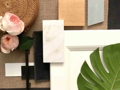 Flat lay of design elements including a white cabinet door, marble sample, pink roses, a green monstera leaf, and woven textures