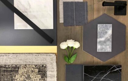 Flat lay of dark and light stone samples, fabric swatches, black hardware, a textured rug, and white flowers