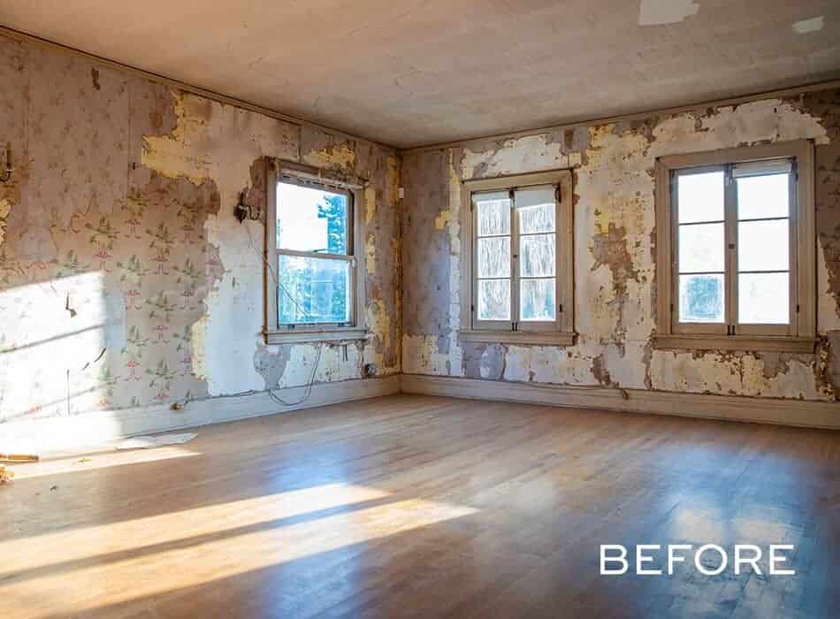 Empty room with peeling wallpaper, wooden floors, and three large windows