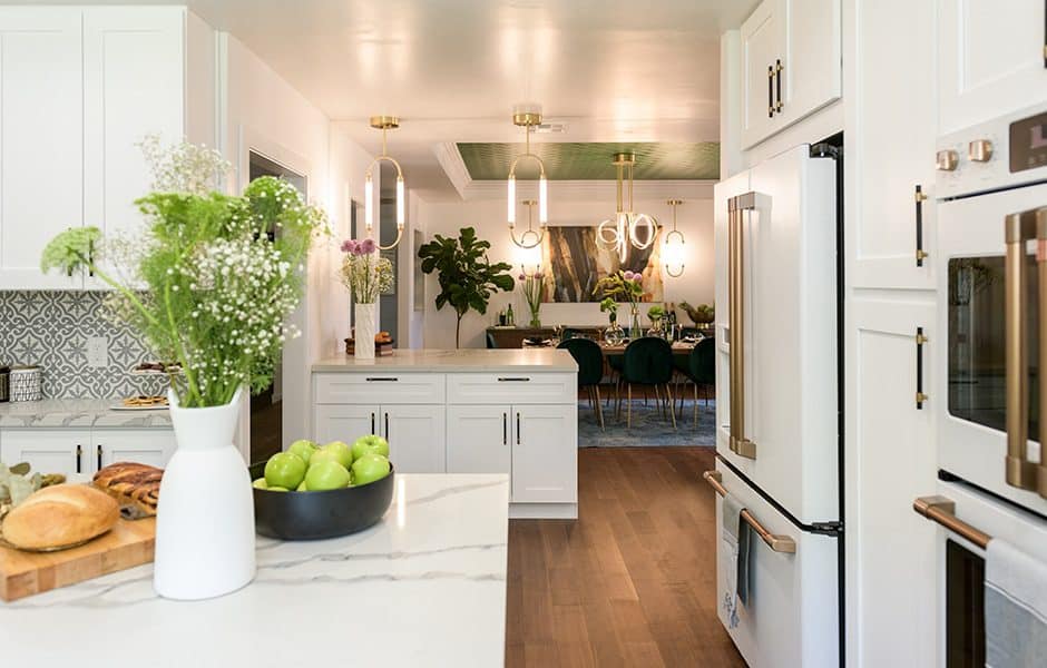 Modern kitchen with white cabinets, stainless steel appliances, light wood floors, marble island, and an open dining room view