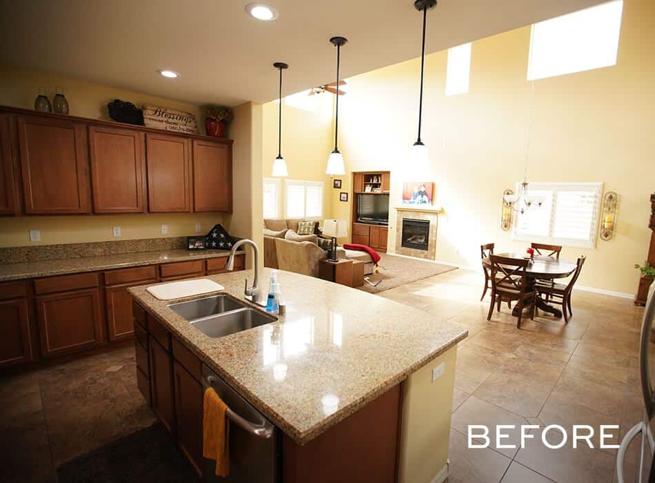 Before image of an open-concept kitchen with granite countertops, wooden cabinets, and pendant lights overlooking a living and dining area