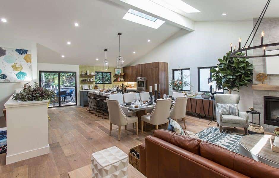 Modern open-concept living and dining area with skylights, wood flooring, a large dining table, and cozy seating by the fireplace