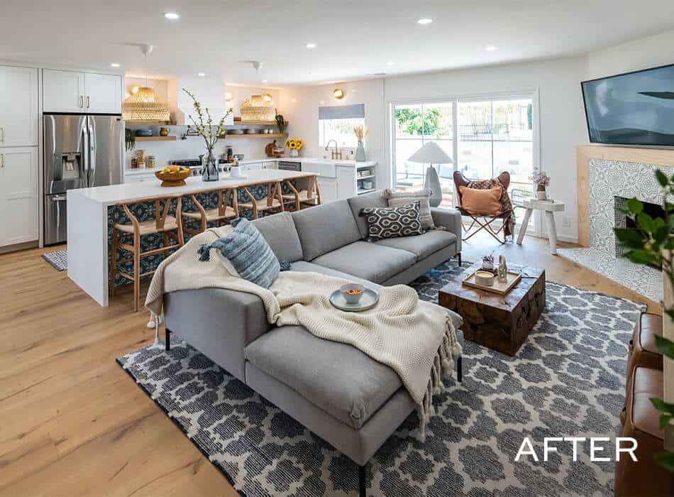 After image of a living room and kitchen with white cabinets, island, gray sectional sofa, coffee table, tiled fireplace, and window to patio