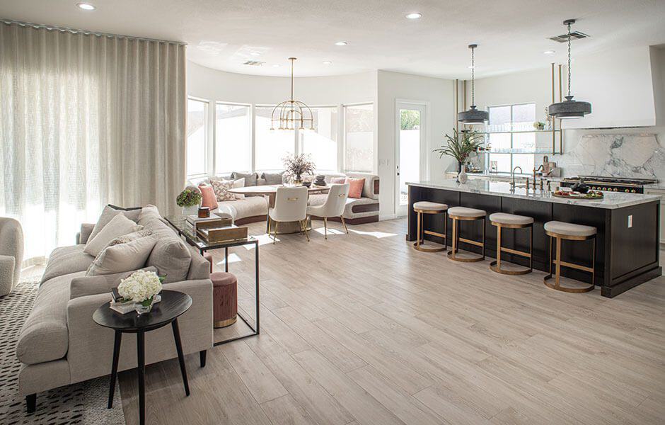 Open-concept living space with neutral-toned furniture, large kitchen island, bay window seating, and light wood floors