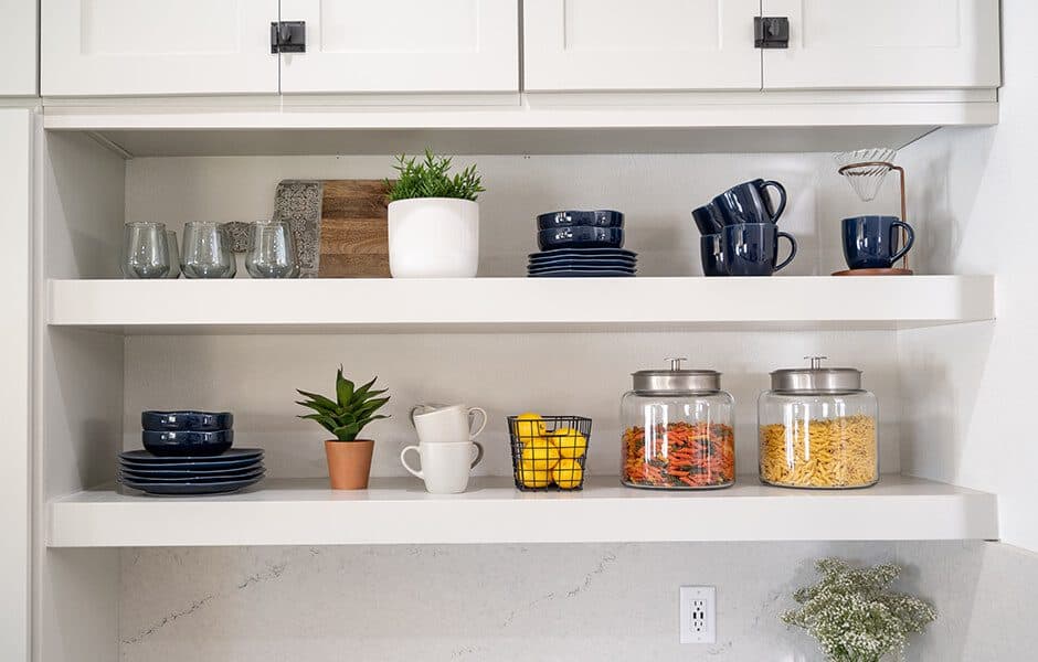 White kitchen shelves with neatly organized dishes, glassware pantry jars, and decorative plants