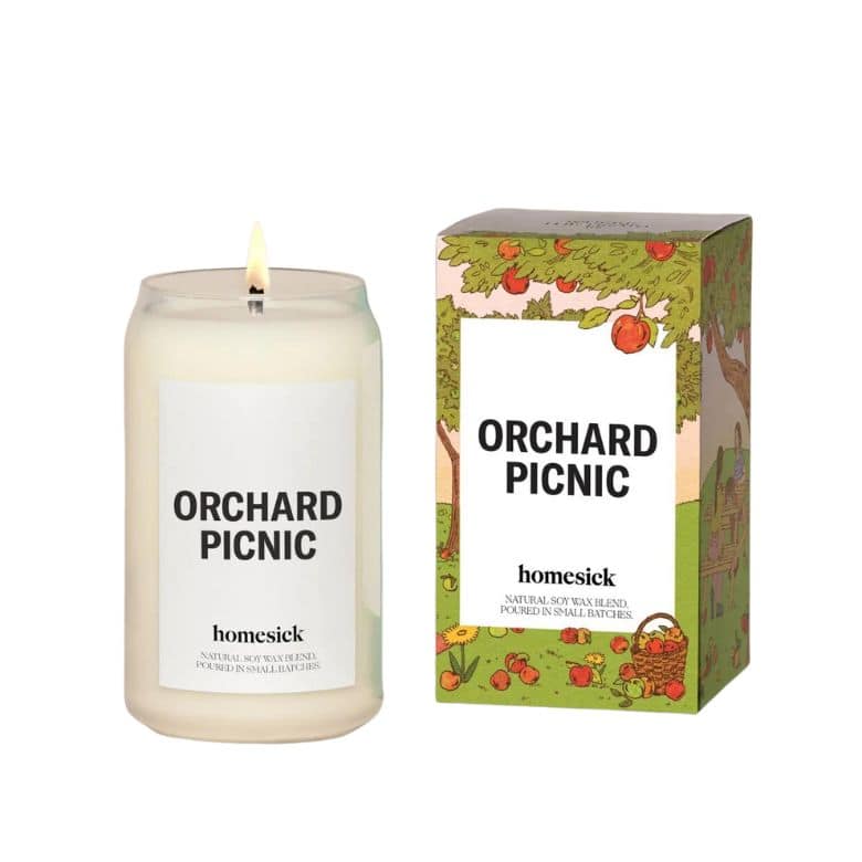 Homesick “Orchard Picnic” candle with illustrated packaging featuring apple trees and a picnic scene