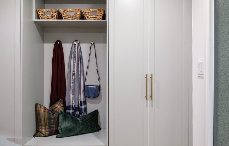 Organized entryway nook with hooks for scarves and bags, a bench with pillows, and woven baskets on a shelf