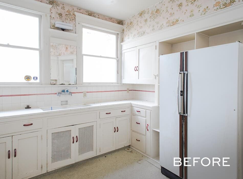 Outdated kitchen with white cabinets, floral wallpaper, and an old refrigerator