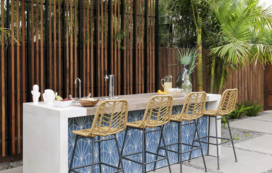 An outdoor kitchen and bar area with a white countertop, a blue tiled backsplash, and a wooden slat fence