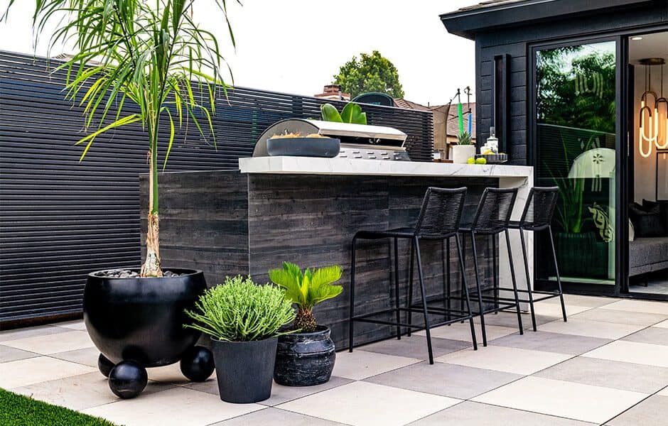 Outdoor kitchen with bar seating, potted plants, and sleek grill station