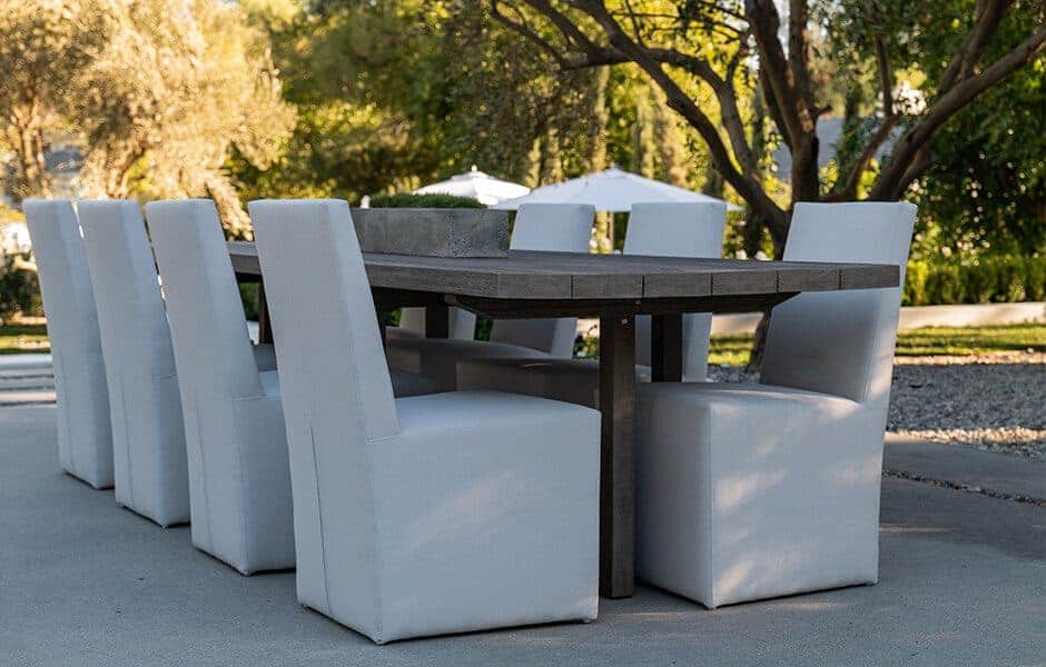 Outdoor dining set with a dark wooden table and eight white cushioned chairs on a patio