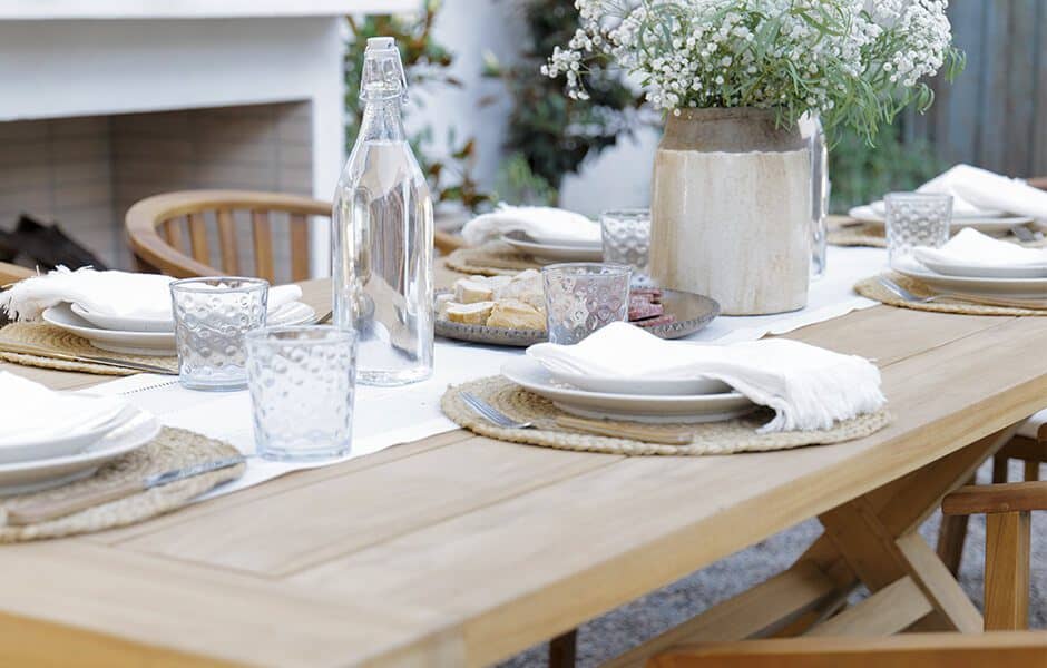 Outdoor dining table with wooden chairs, table setting, flowers, and fireplace.