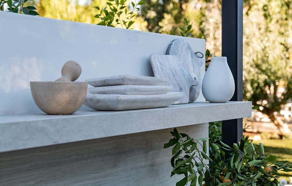 Outdoor stone shelf with marble trays, a mortar and pestle, cutting boards, and a white vase