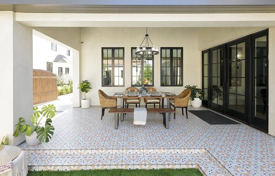 Covered outdoor dining area with patterned tile floor, rattan chairs, wood table, bench seating, and potted plants