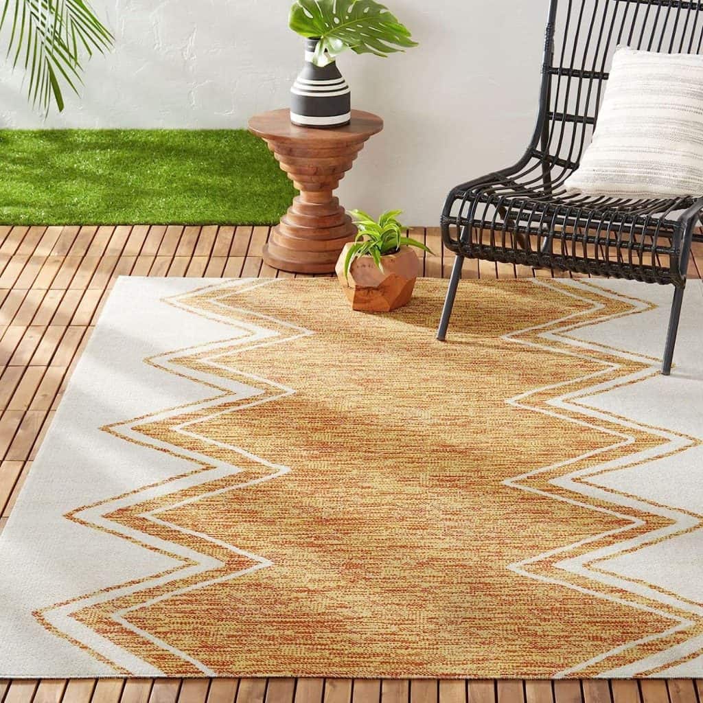 Outdoor rug with zigzag pattern in a patio setup featuring wood slat flooring and woven black chair