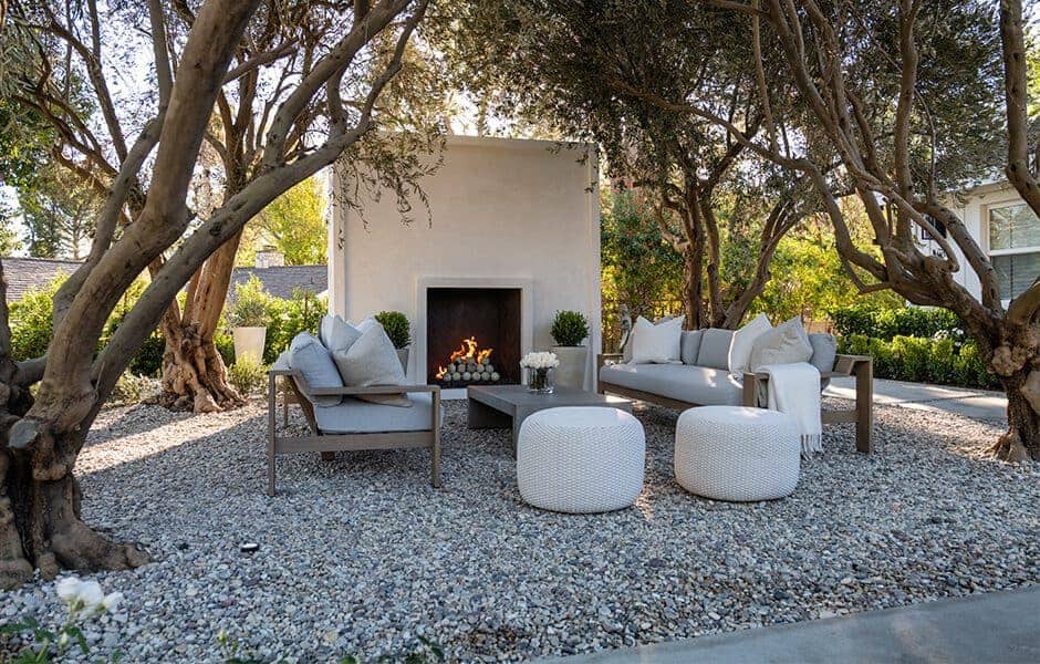 Outdoor seating area with modern sofas, round ottomans, a fireplace, and trees providing shade