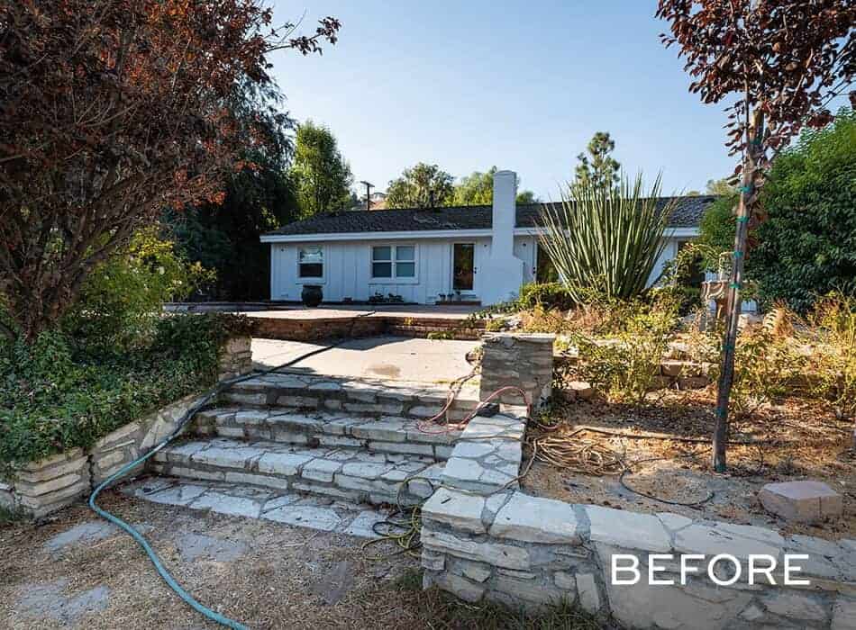 Front yard with stone steps, overgrown plants, and a white house in the background