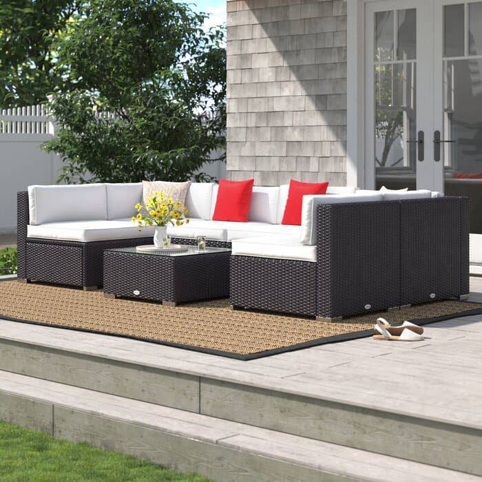 Wicker patio sectional with white cushions, red accent pillows, and a central coffee table on a tan outdoor rug
