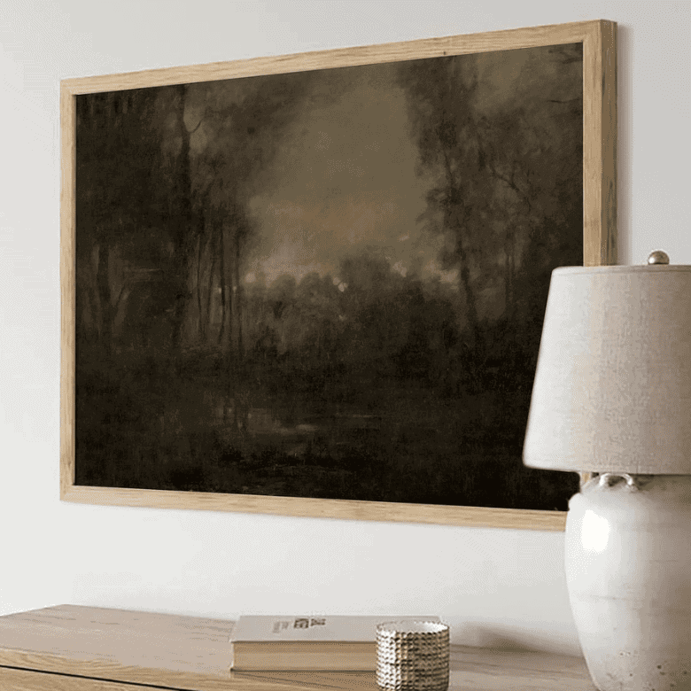 Framed dark landscape painting above a console with a lamp and decor items.