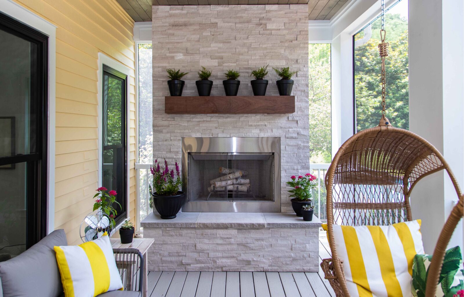 Cozy screened porch with stone fireplace, potted plants, and wicker swing chair