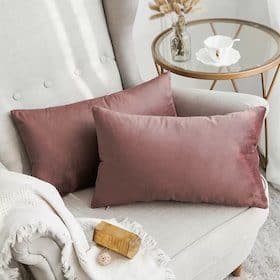 Two mauve rectangular throw pillows placed on a light beige tufted armchair with a white fringed blanket
