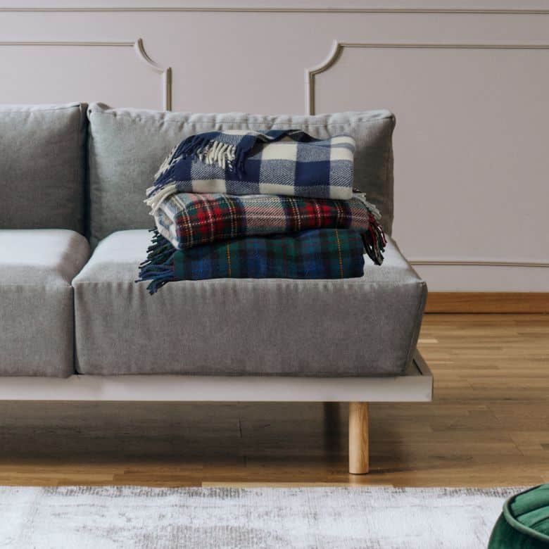 Three plaid blankets stacked on a gray sofa